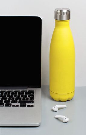 Yellow insulated bottle on grey desk near laptop close up