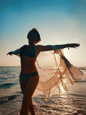 Young woman in white cover up dancing on the beach on  sunsetの写真素材