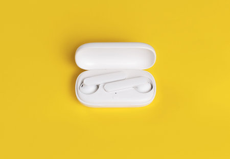 White wireless earphones with case on yellow background close up