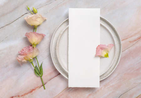 Wedding menu laying on a ceramic plate on a marble table decorated with flowers and ribbons. Mock-up scene with blank paper greeting cards. Feminine flat layの写真素材