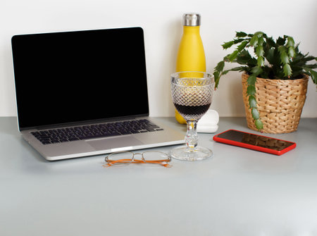 Smart working workspace - laptop, insulated bottle, plant, cell phone, glasses and a glass of wine on grey desk close upの写真素材