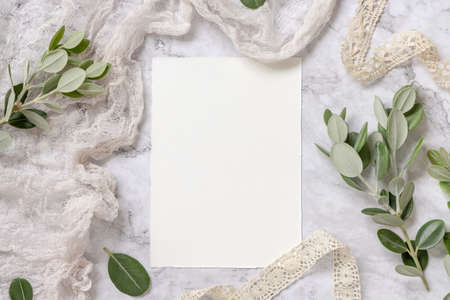 Blank paper card laying on a marble table decorated with eucalyptus branches and ribbons. Mock-up scene with wedding paper invitation card. Elegant feminine flat layの写真素材