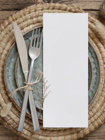 Blank menu card on plate with fork and knife on wooden table with bohemian decorations and dried plants, top view. Boho wedding card mockupの写真素材