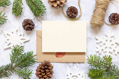 Winter Christmas Composition with a card over sealed envelope flat lay. Christmas and New Year greeting card template with fir tree branches, pine cones, snowflakes and rope on marble background top view. Holiday mockup.の写真素材