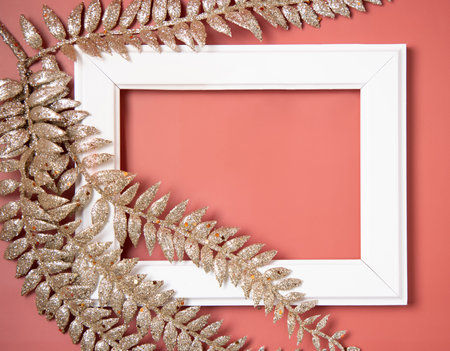 White frame covered and decorated with Christmas golden leaves on pink background top view