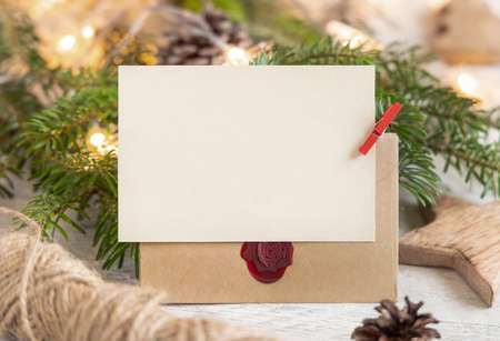 Winter Composition with a blank card, sealed envelope and fir branches close up. Christmas and New Year greeting card template with lights background. Holiday mockup.の写真素材
