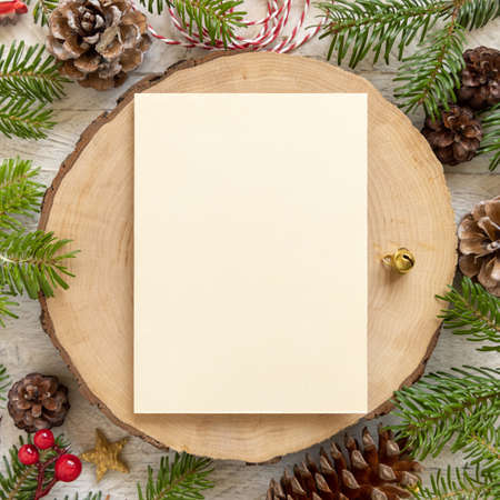 Winter Christmas Composition with a blank card over wooden table flat lay. Christmas and New Year greeting card template with fir tree branches, pine cones and decorations top view. Holiday mockup.の写真素材