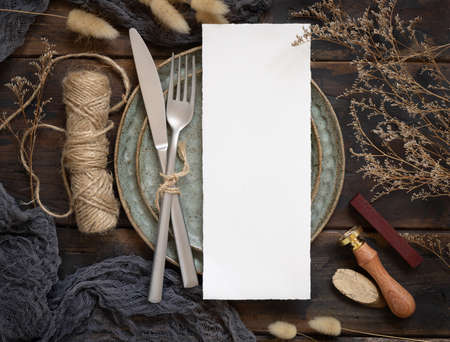 Blank menu card on plate with fork and knife on wooden table with bohemian decorations and dried plants, top view. Boho wedding invitation card mockupの写真素材