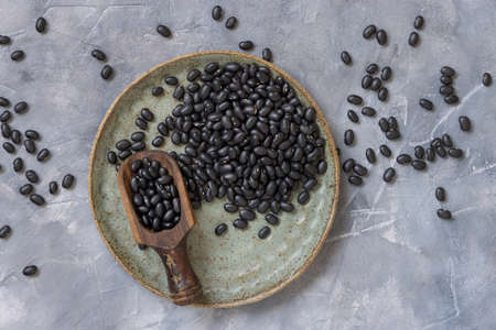 Ceramic plate full of dry black beans with a wooden scoop on grey table top view with negative space. Healthy eating and vegetarian concept. Traditional Latin American cousin ingredientの写真素材