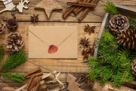 Winter Christmas Composition with a sealed envelope over wooden table flat lay. Christmas and New Year greeting card template with fir tree branches, pine cones and Chritmas decorations top view. Holiday mockupの写真素材