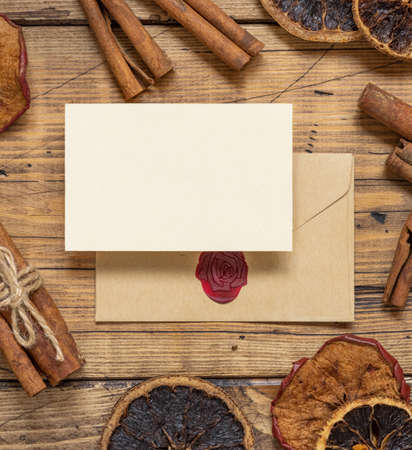 Winter Composition with a blank card and sealed envelope, spices and dried fruits  on wooden table flat lay. Christmas and New Year greeting card template with dried fruits and spices top view. Holiday mockupの写真素材