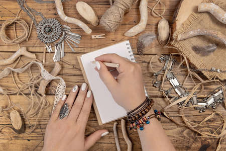 Woman hands writing in textbook on wooden table with ethnic jewelry and natural decor top viewの写真素材