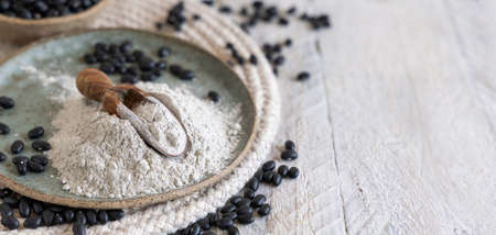 Ceramic plate with black beans flour and dried beans with a wooden spoon closeup with copy space. Healthy eating and vegetarian concept. Traditional Latin American cousin ingredientの写真素材