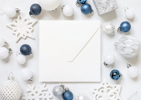 Blank square envelope with white, blue and silver Christmas decorations top view on white table....