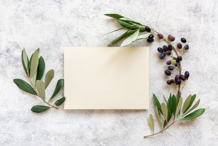 Wedding invitation card laying on a marble table decorated with olive branches top view. Elegant modern template with vertical blank paper card. Mediterranean flat lay mockup with place for textの写真素材