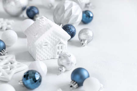 White toy house with blue, white and silver Christmas decorations closeup on white table. Monochrome winter compositionの写真素材