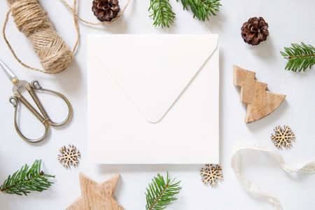 Winter Christmas Composition with a card over sealed envelope flat lay. Christmas and New Year greeting card template with fir tree branches and pine cones on white wooden background top view. Holiday mockup.の写真素材