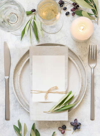 Wedding Table place with place card and porcelain plates decorated with olive branches top view. Elegant modern template with vertical blank paper card flat lay. Mediterranean mockup, copy spaceの写真素材