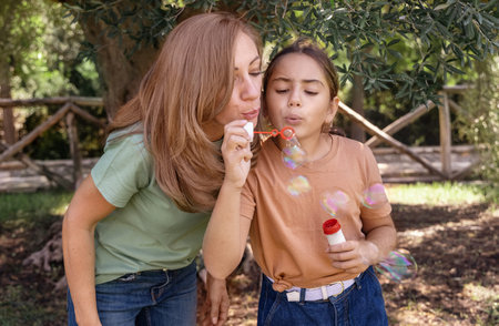Mother and daughter blowing soap bubbles outdoors. Cute kid girl and middle aged woman having fun in a park in summer. Children outdoor activity concept, authentic childhood momentの写真素材