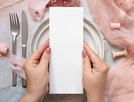 Hand with a menu card over wedding table place on a marble near dried pink flowers and silk ribbons...