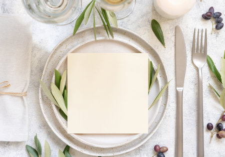 Wedding Table place with invitation card and porcelain plates decorated with olive branches top view. Elegant modern template with square blank paper card flat lay. Mediterranean mockup, copy spaceの写真素材