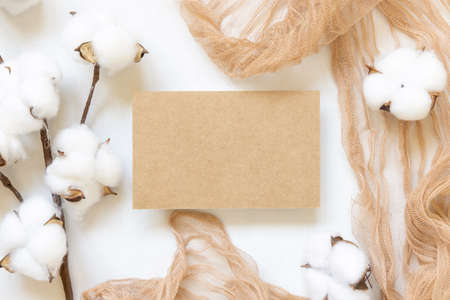 Feminine Wedding card mockup on white table with cotton flowers top view. Elegant modern template with horizontal blank paper card, flat lay with place for text.  Minimalistic stationery scene. Natural, eco-friendly conceptの写真素材