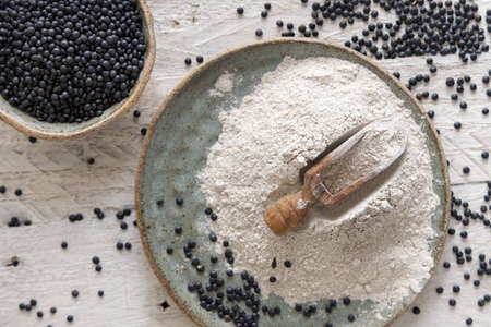 Plate with a scoop of black lentils flour and beans on white wooden table top view.  Alternative flour, healthy eating and vegetarian concept. Traditional Asian and North African cuisines ingredientの写真素材