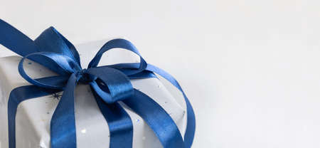 Grey Wrapped Christmas present with a blue ribbon bow on grey close up with copy space. Grey and blue winter composition with Gift box, copy spaceの写真素材