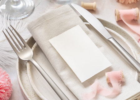 Wedding Table place with a paper card over napkin near flowers, silk ribbons and feathers  close up....