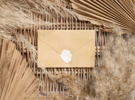 Boho sealed envelope on a wattled table with dry palm leaves and pampas grass top view. Bohemian tropical scene with blank horizonal envelope mockup, place for textの写真素材