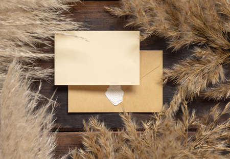 Wedding paper card  and envelope near dried pampas grass on dark brown wood top view. Bohemian mockup scene with blank horizontal card flat lay, place for textの写真素材