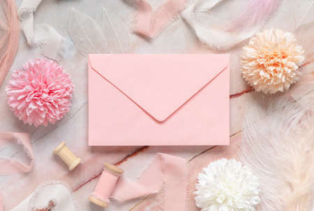 Pink envelope between pastel flowers, silk ribbons and feathers on marble top view. Romantic scene with rectangular blank envelope mockup flat lay,  place for text. Valentines, Spring or girlish conceptの写真素材