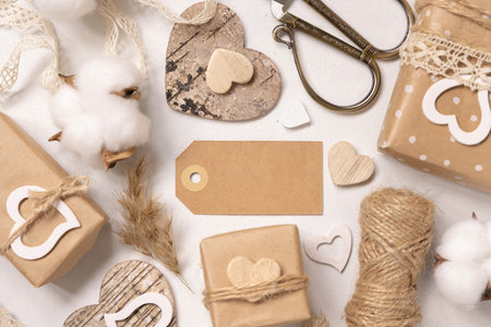 Kraft paper gift tag between Valentines present, wooden hearts and dried flowers top view. Spring scene with horizontal blank label. Rustic, cottage chic or bohemian mockup, copy spaceの写真素材