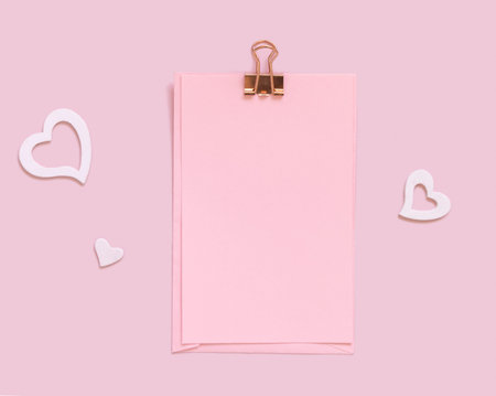 Pink paper card with clip near white hearts on pink top view. Minimal scene with blank card mockup,...