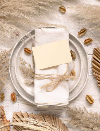 Wedding table place with horizontal blank card  on white wooden table top view. Boho card mockup. Tropical beige template with dried plants, palm leaves and pampas grassの写真素材