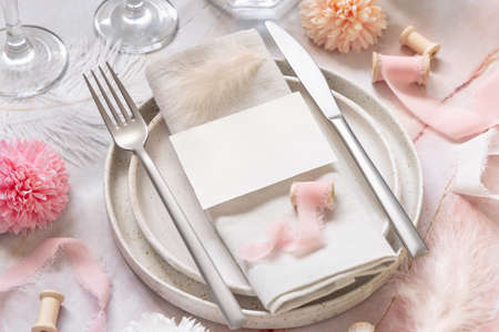 Wedding Table place with a paper card over napkin near flowers, silk ribbons and feathers closeup. Romantic template with blank card on a plate flat lay. Vertical card mockup, copy spaceの写真素材