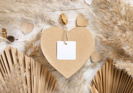 Heart shaped Valentines present with square blank gift tag near dried pampas grass, palm leaves and hearts top view. Rustic, cottage chic or bohemian label mockup, copy spaceの写真素材