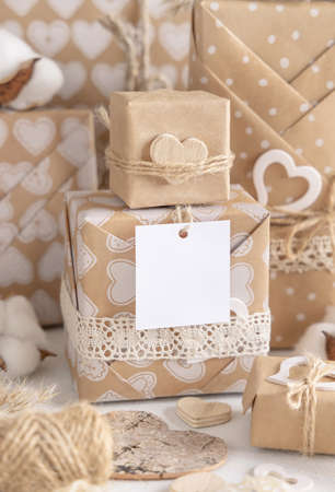 Valentines kraft paper wrapped presents with square gift tag and hearts close up. Spring scene with blank label. Rustic, cottage chic or bohemian mockup, copy spaceの写真素材