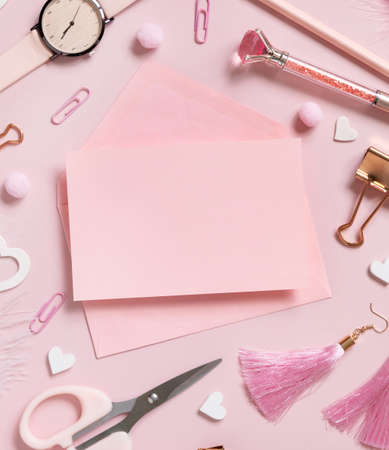 Pink paper card with envelope, school accessories and hearts on pastel pink top view, blank card mockup. Girly workplace. Back to school and valentines day conceptsの写真素材