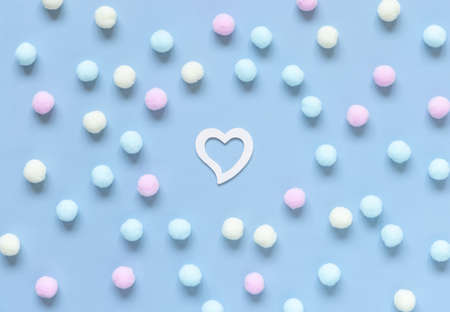 White heart between pastel pompoms on light blue top view. Minimal scene for Valentines day, wedding and girly concept.の写真素材