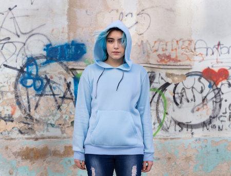 Teenager wearing light blue oversize hoodie and jeans looking into the camera. Blue haired teen girl stays outdoors against graffiti wall. Clothing mockupの写真素材