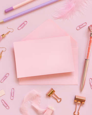 Pink paper card with envelope near school accessories and stationery on pastel pink background Top view. Girly mockup with pencils, pens,  clips and feathers. Back to school and girly conceptの写真素材