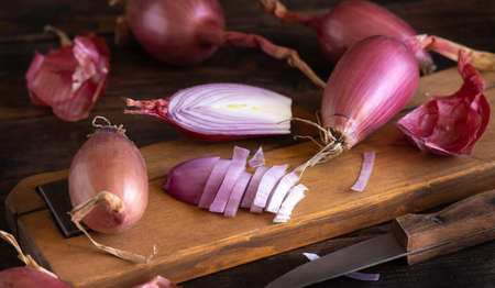 Sliced Red tropea onions with a knife on a wooden board close up. Traditional local south italian vegetable. Cooking process in home kitchenの写真素材