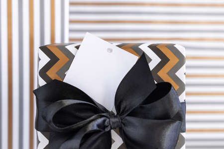 Present with blank square gift tag and black bow close up. Gift boxes wrapped in Striped and chevron geometric paper. Christmas, New Year, Birthday, Anniversary label mockupの写真素材
