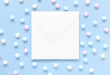 Blank envelope between pastel pom-poms on light blue top view. Romantic scene with blank horizontal...