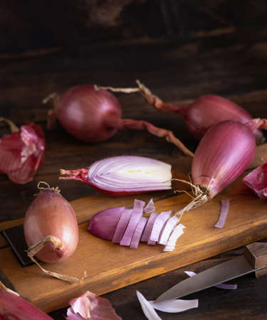 Sliced Red tropea onions with a knife on a wooden board close up. Traditional local south italian vegetable. Cooking process in home kitchenの写真素材