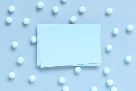 Blank card between pastel pom-poms on light blue top view. Romantic scene with blank horizontal card with place for text flat lay.  Spring or boyish conceptの写真素材
