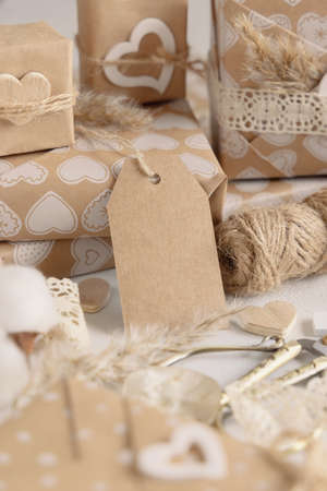 Valentines wrapped presents with vertical gift tag close up. Spring scene with blank label. Rustic, cottage chic or bohemian mockup, copy spaceの写真素材