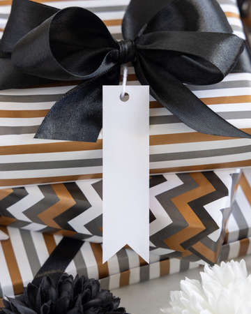 Present with blank vertical gift tag and black bow close up. Gift boxes wrapped in Striped and chevron geometric paper near black and white decor. Christmas, New Year, Birthday, Anniversary label mockupの写真素材