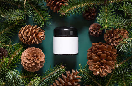 Brown glass jar near fir branches and pine cones on dark green top view. Brand packaging mockup. Skincare beauty product, cream or serum. Healthcare natural cosmetics conceptの写真素材